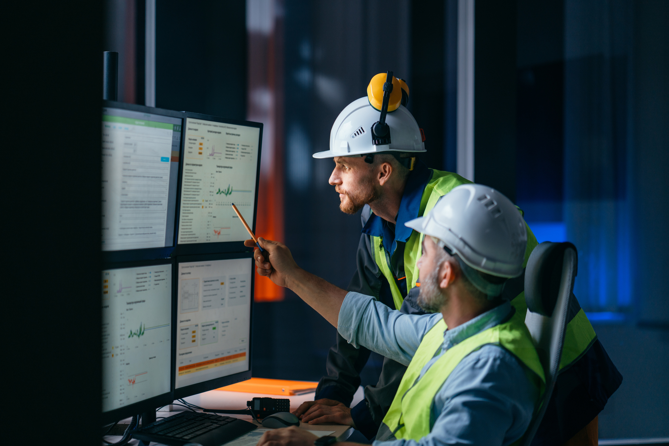 Two plant personnel reviewing maintenance data on control room monitors